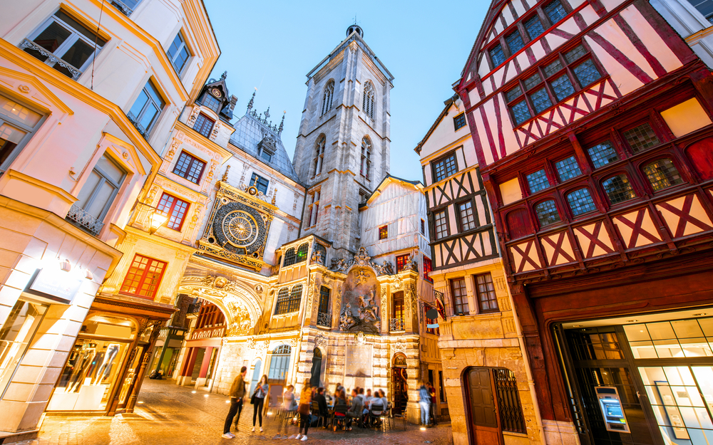 Straßenansicht mit beleuchteten Gebäuden und dem berühmten Uhrturm in der Dämmerung in der Altstadt von Rouen in Frankreich