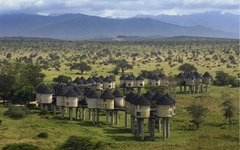 Erhöhtes Hotel in Kenia mit runden Hütten, umgeben von grüner Landschaft und Bergen im Hintergrund.
