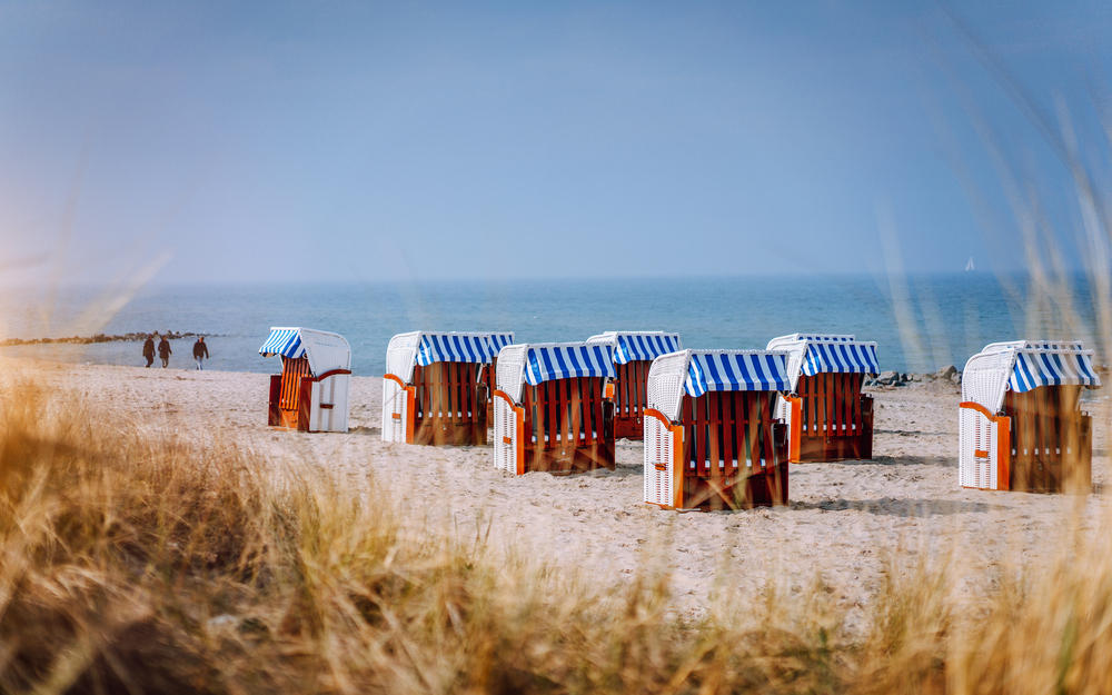 Blue striped roofed chairs on sandy beach on sunny day framed by dune grass in Travemunde. Germany